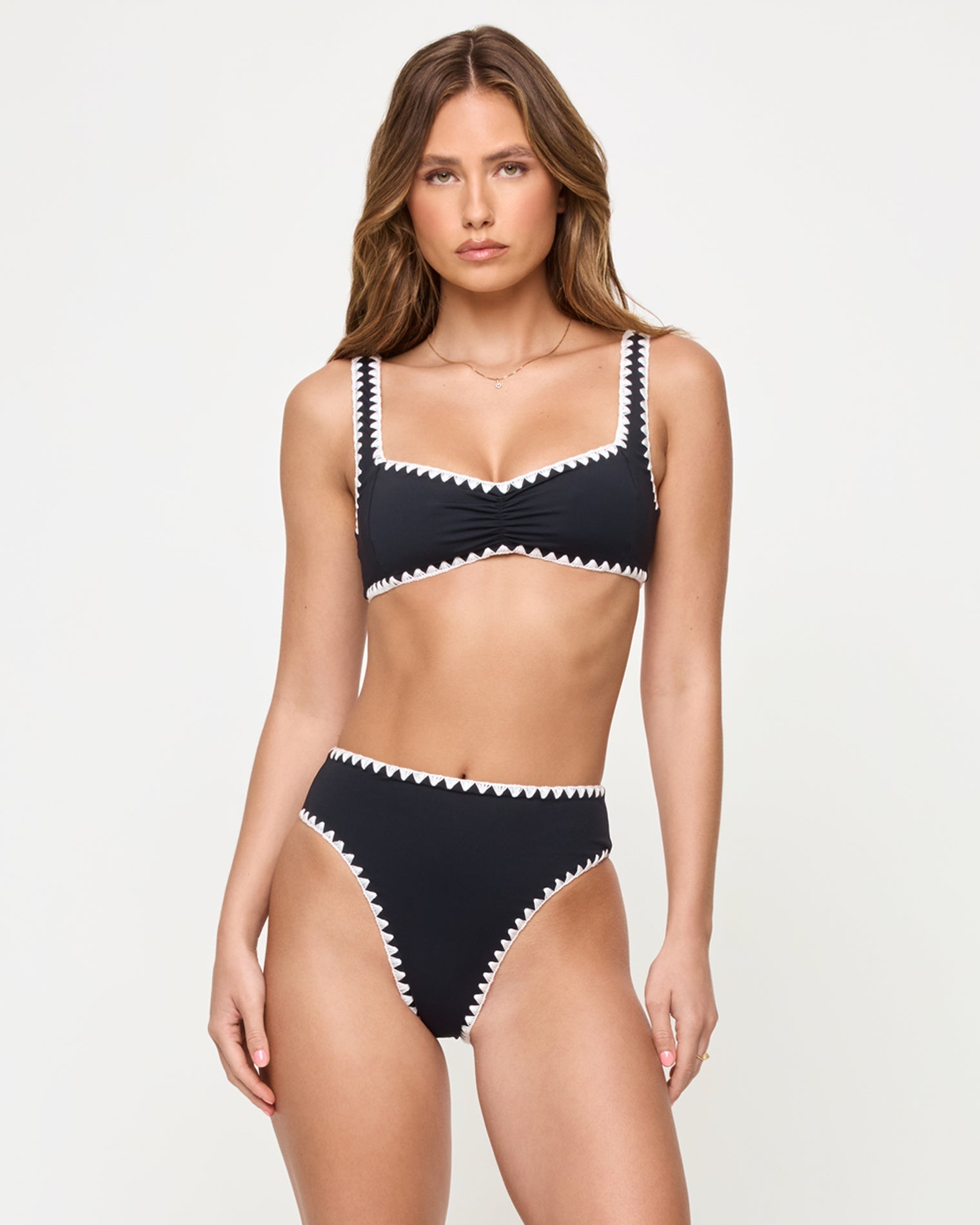 front view of woman wearing a black bikini with white trim on a plain background