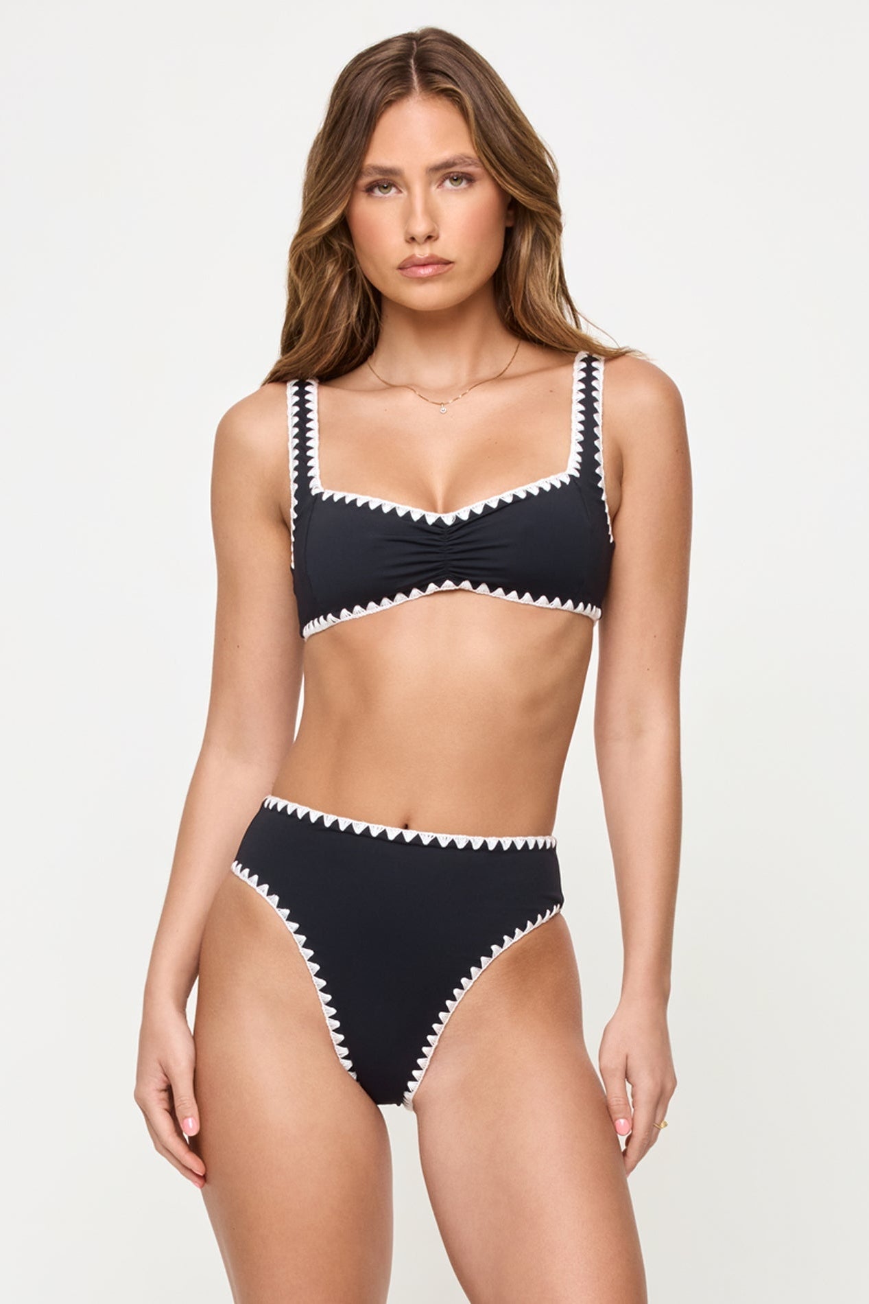 front view of woman wearing a black bikini with white trim on a plain background