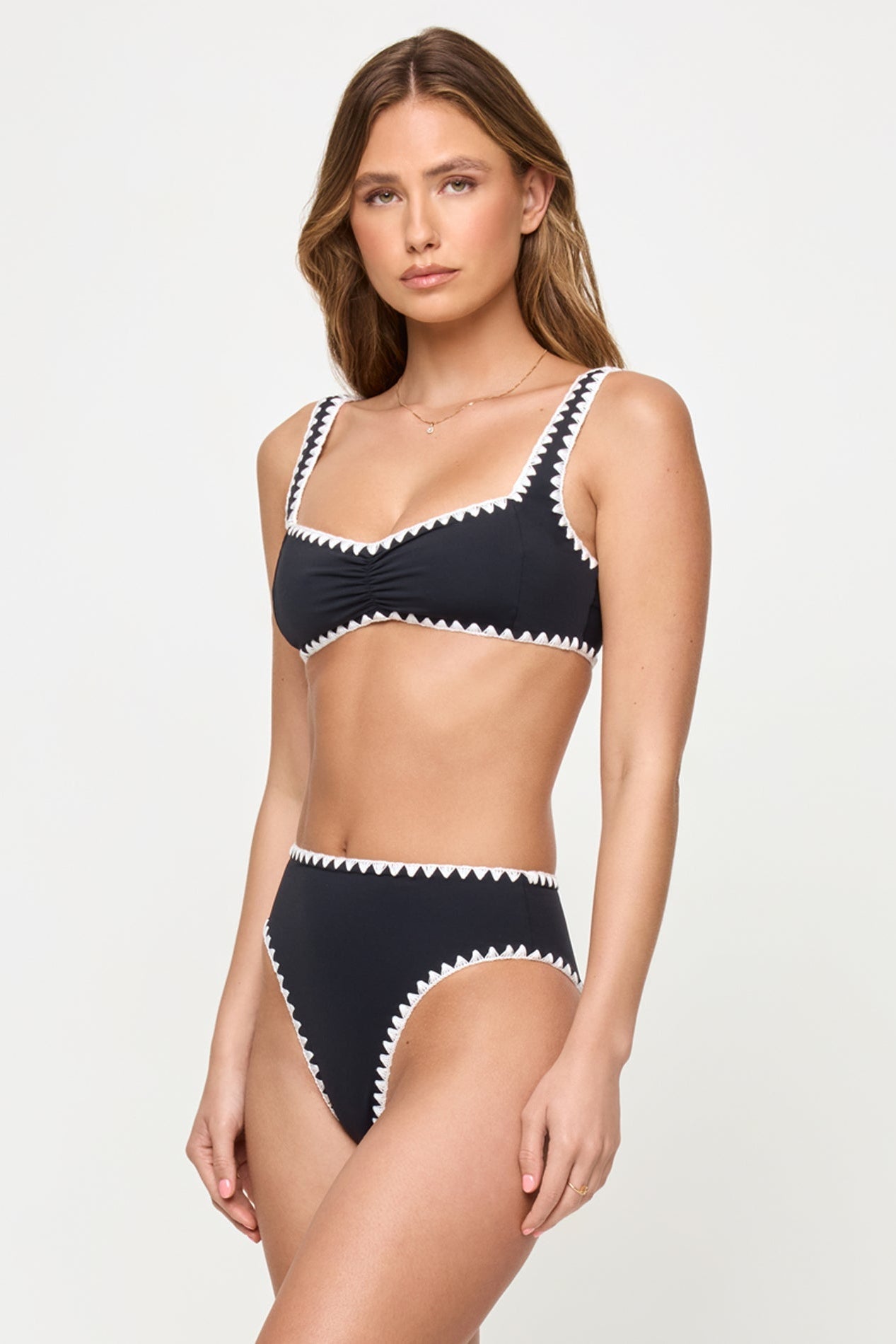 side view of woman wearing a black bikini with white trim on a plain background