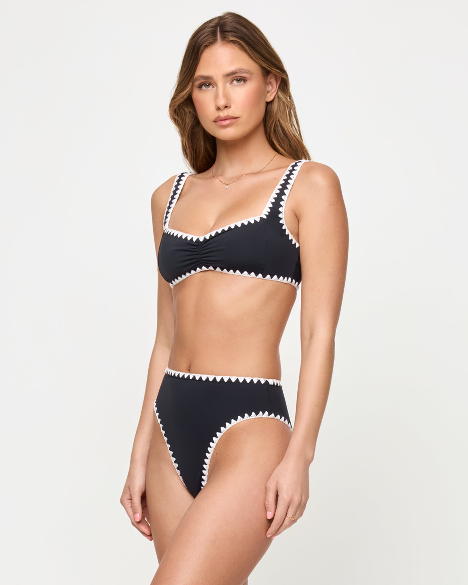 side view of woman wearing a black bikini with white trim on a plain background
