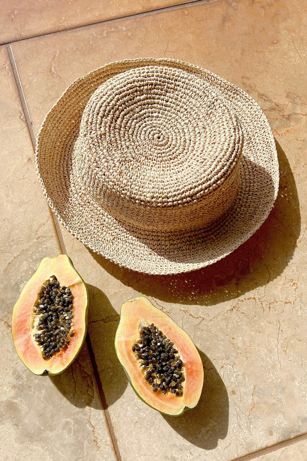Flat lay of the Isadora Bucket Hat in natural styled with tropical fruits on a terracotta tile.