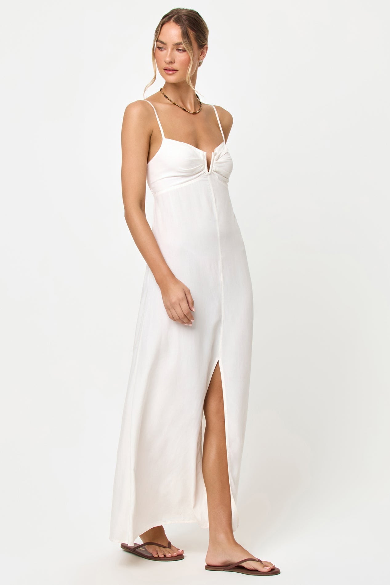 Woman wearing a white maxi dress with a high slit on a white background