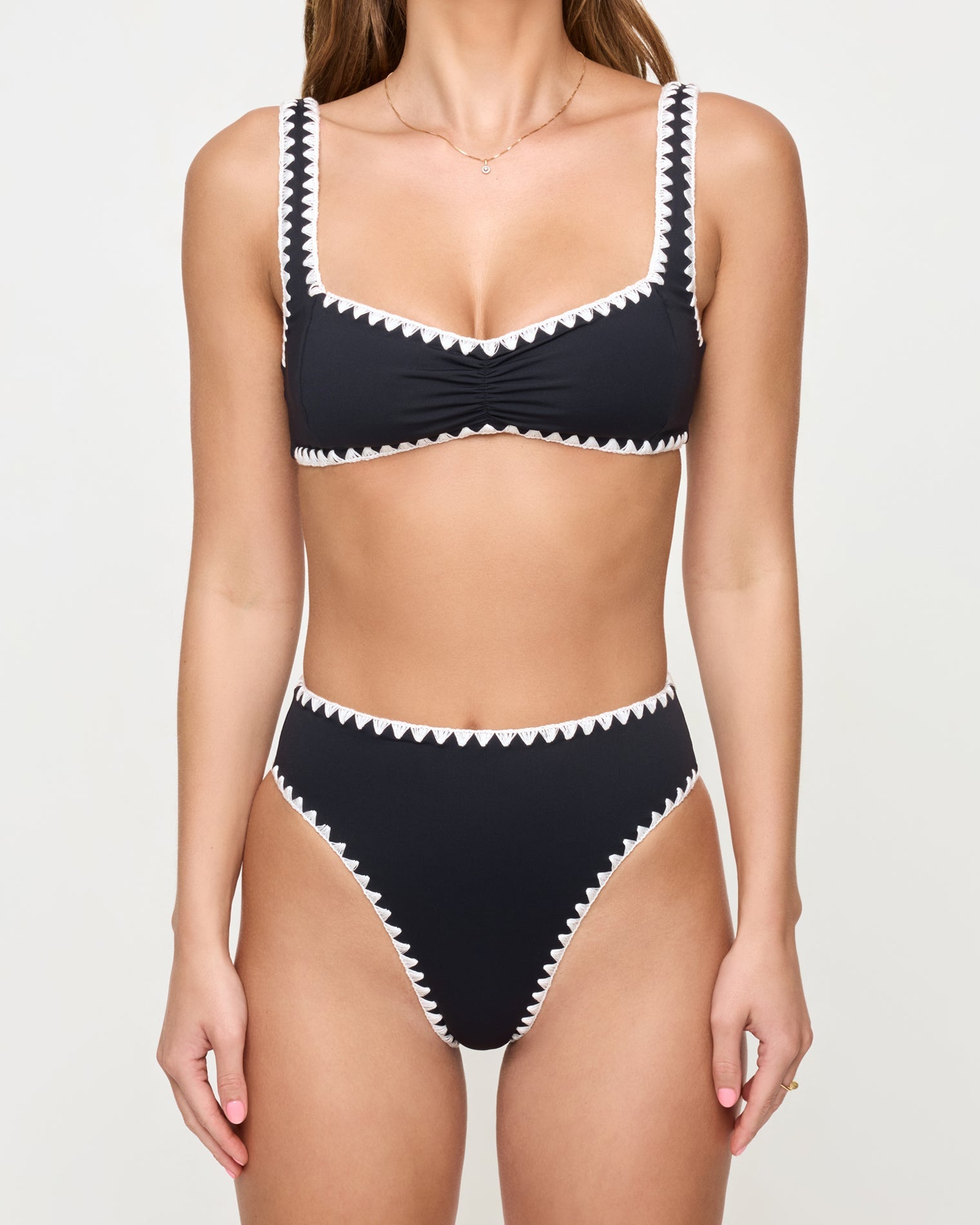 close up view of woman wearing a black bikini with white trim on a plain background